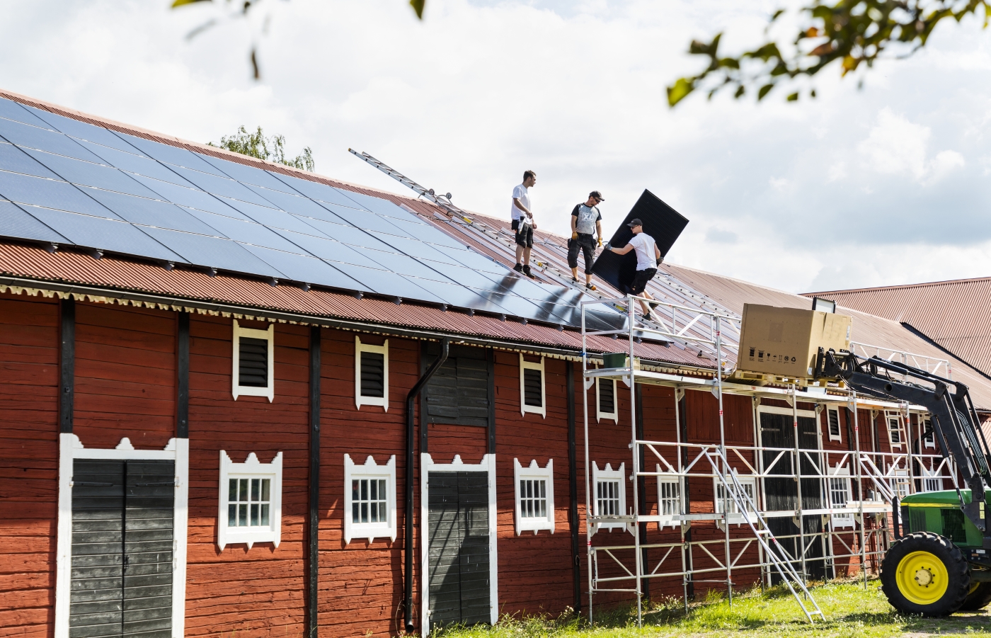 Tre personer står på taket till en stor lada och monterar solpaneler