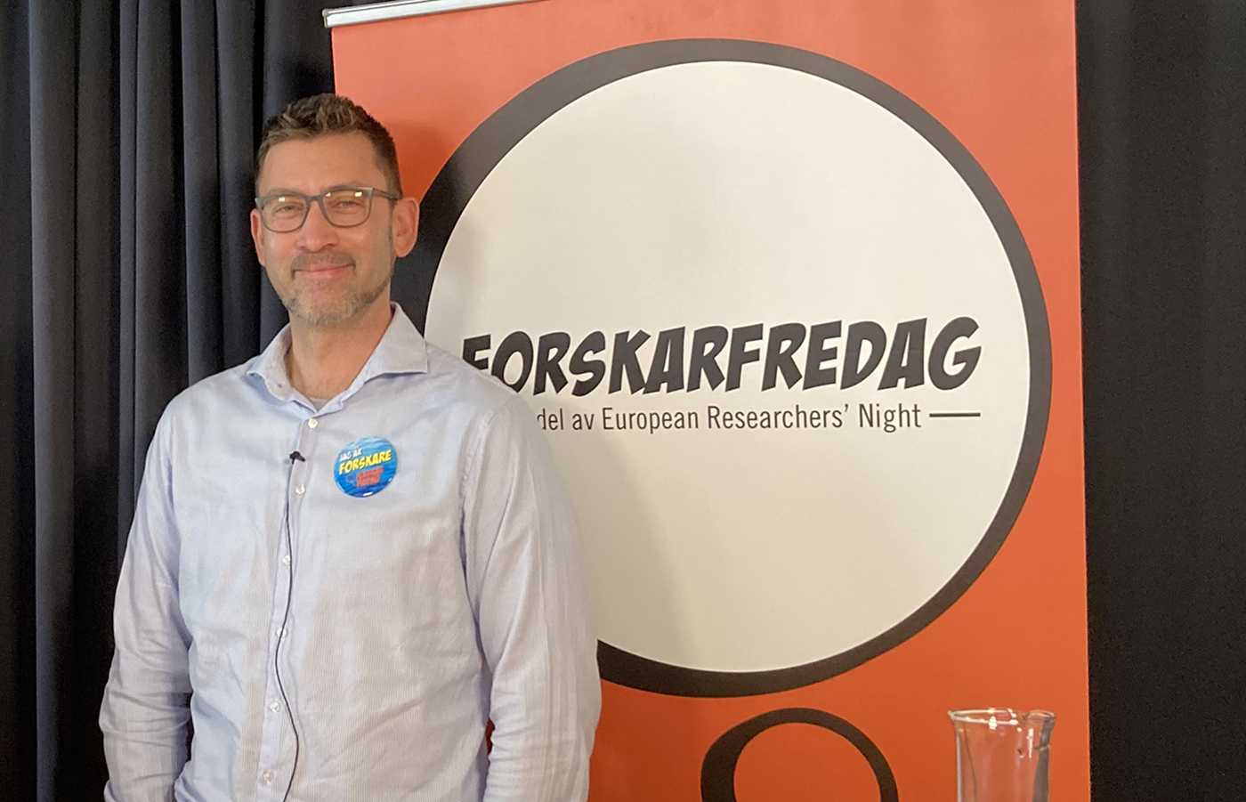 A man stands beside a poster saying ForskarFredag