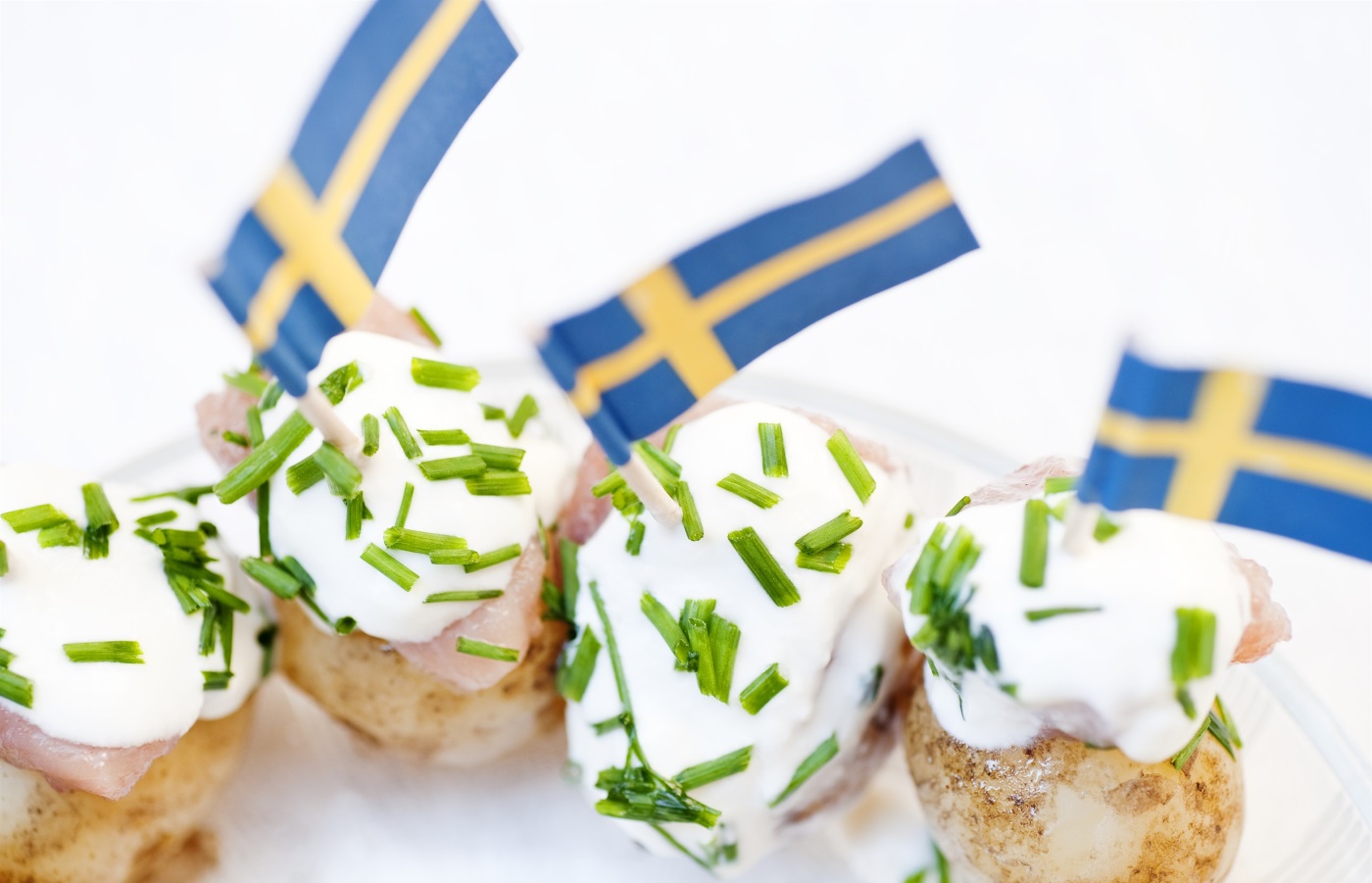 Fyra potatisar med gräddfil, räkor och gräslök, dekorerade med svenska flaggor