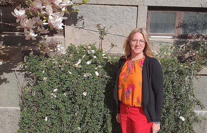 Anna-Karin Krijger står framför en husfasad bredvid ett magnolia träd. Hon tittar in i kameran och ler.